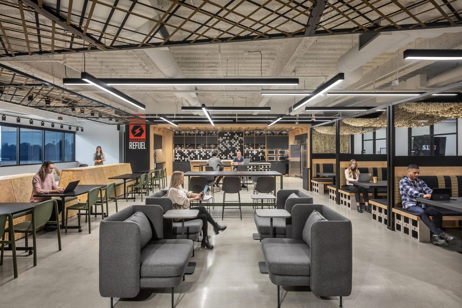 Image shows open and collaborative working space. The space has an industrial feel with multiple couches, chairs, tables and many coworkers collaborating.