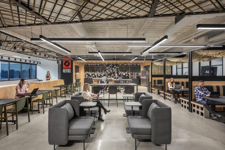 Image shows open and collaborative working space. The space has an industrial feel with multiple couches, chairs, tables and many coworkers collaborating.